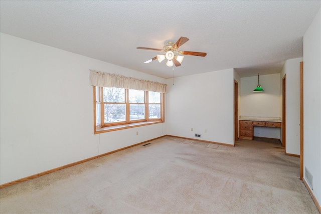 carpeted spare room featuring ceiling fan, built in desk, and a textured ceiling