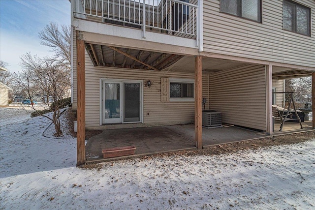 snow covered house with central AC unit and a patio