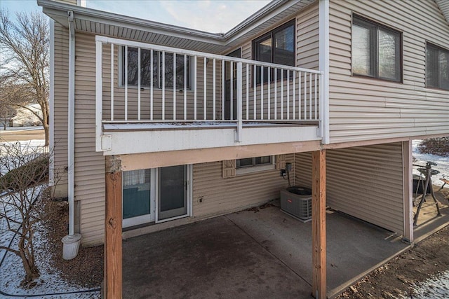 snow covered rear of property featuring cooling unit, a patio, and a balcony