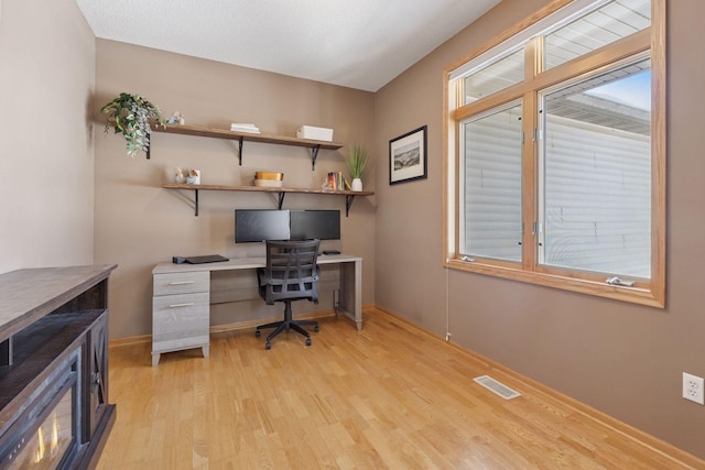 home office featuring light wood-style flooring, a healthy amount of sunlight, visible vents, and a wood stove