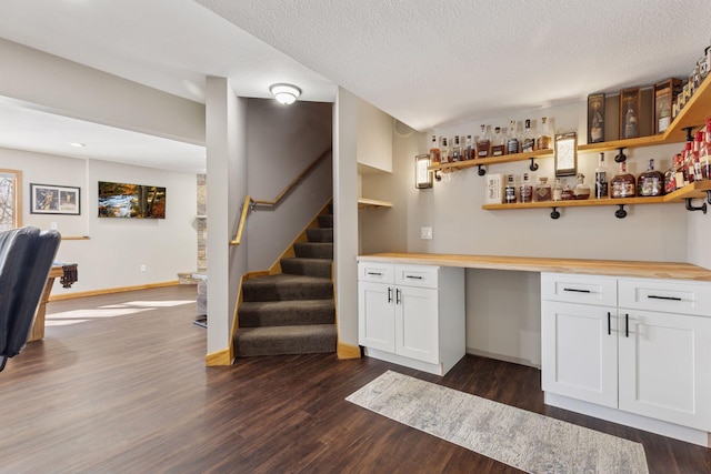 bar with dark wood-type flooring, baseboards, stairway, a textured ceiling, and a bar