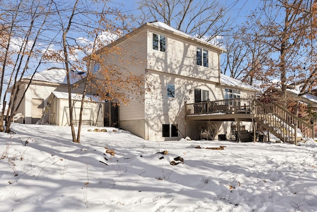 snow covered property featuring a wooden deck, an outbuilding, stairs, and a shed