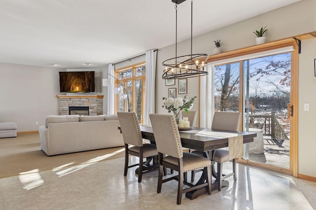 dining area with a stone fireplace, baseboards, a notable chandelier, and a healthy amount of sunlight