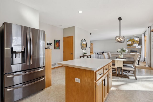 kitchen with a notable chandelier, a kitchen island, open floor plan, stainless steel fridge, and light countertops