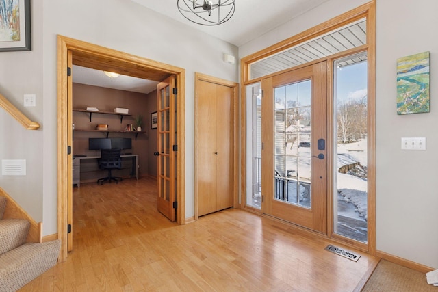 entryway with visible vents, baseboards, light wood-type flooring, stairs, and a notable chandelier