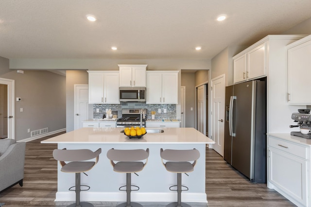 kitchen featuring a breakfast bar, a kitchen island with sink, stainless steel appliances, white cabinets, and decorative backsplash