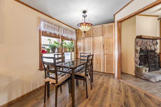 dining area with ornamental molding, a stone fireplace, and hardwood / wood-style floors