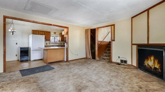 unfurnished living room featuring light colored carpet, sink, and a textured ceiling