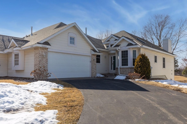 view of front of house featuring brick siding, driveway, a chimney, and an attached garage