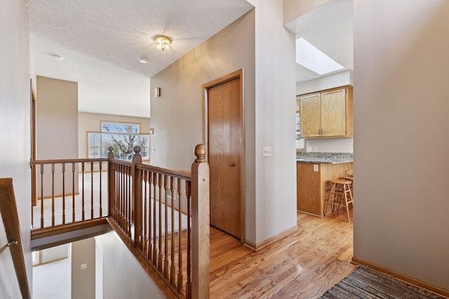 corridor featuring baseboards, an upstairs landing, light wood-type flooring, and a textured ceiling