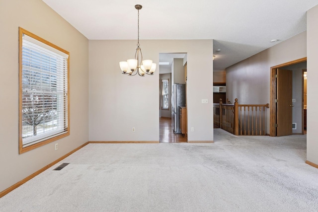 carpeted empty room featuring an inviting chandelier, baseboards, and visible vents