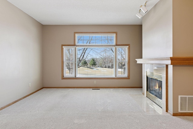 unfurnished living room with baseboards, visible vents, a fireplace with flush hearth, a textured ceiling, and light carpet