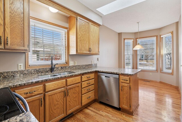 kitchen with light wood-style flooring, a sink, a peninsula, a skylight, and dishwasher