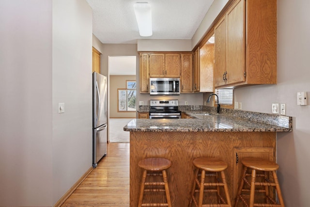 kitchen featuring a sink, a kitchen breakfast bar, light wood-style floors, appliances with stainless steel finishes, and a peninsula