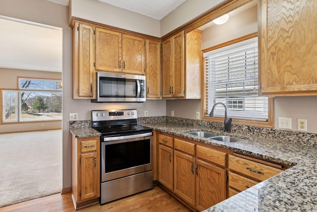 kitchen featuring light wood-style flooring, a sink, appliances with stainless steel finishes, brown cabinetry, and stone counters