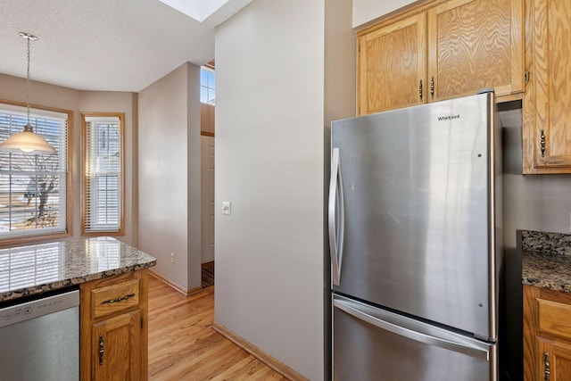 kitchen with baseboards, light stone counters, light wood-style flooring, appliances with stainless steel finishes, and hanging light fixtures