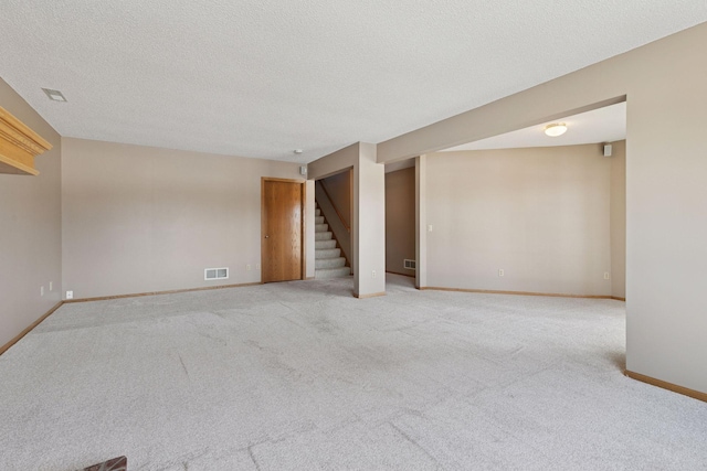 empty room featuring visible vents, baseboards, light colored carpet, stairs, and a textured ceiling