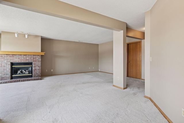 unfurnished living room featuring baseboards, a fireplace, track lighting, a textured ceiling, and carpet flooring