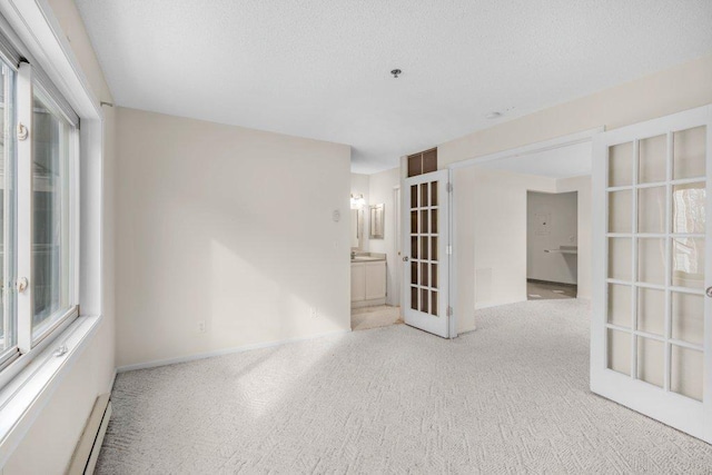 unfurnished room featuring light carpet, baseboard heating, a textured ceiling, and french doors