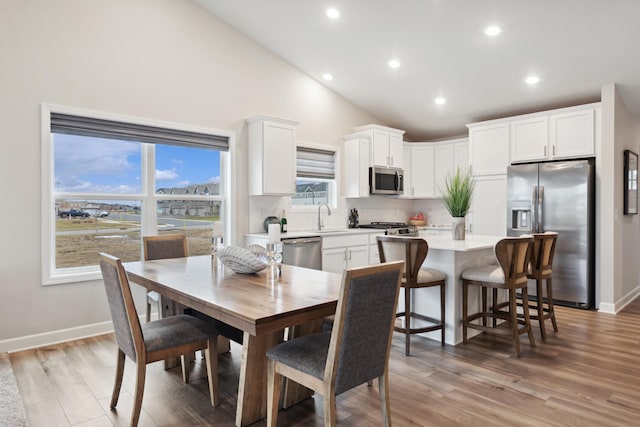 dining area with high vaulted ceiling, sink, and light wood-type flooring