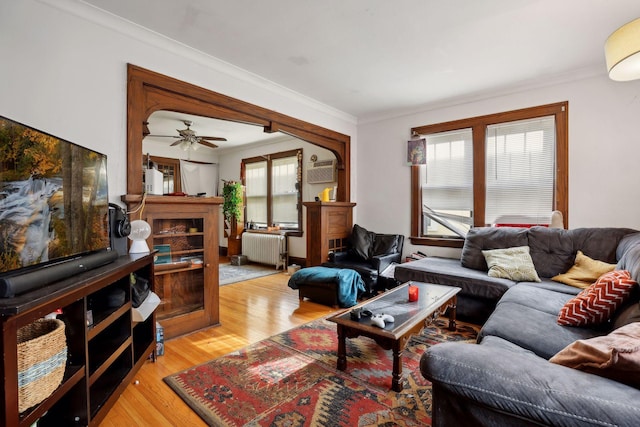 living room with crown molding, radiator heating unit, a wall unit AC, and light wood-type flooring