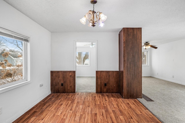 interior space featuring hardwood / wood-style floors, ceiling fan with notable chandelier, wooden walls, and a textured ceiling