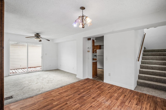 unfurnished living room with hardwood / wood-style floors, ceiling fan with notable chandelier, and a textured ceiling