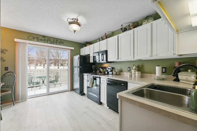 kitchen featuring sink, white cabinetry, black appliances, a textured ceiling, and light wood-type flooring