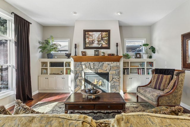 living area with a stone fireplace, dark wood-type flooring, and baseboards