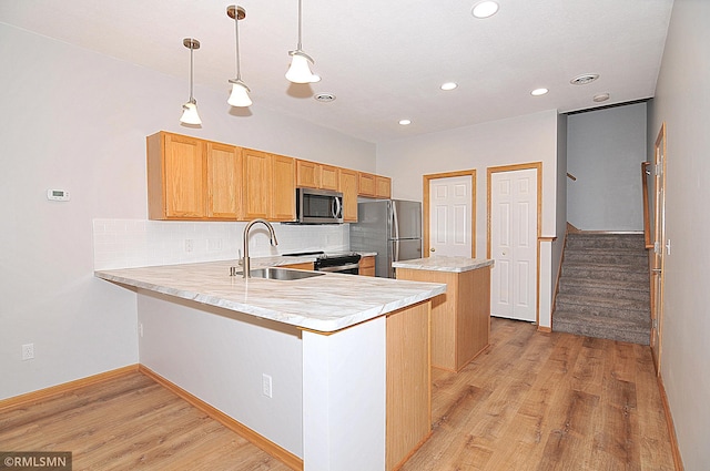 kitchen with pendant lighting, sink, kitchen peninsula, stainless steel appliances, and light hardwood / wood-style flooring