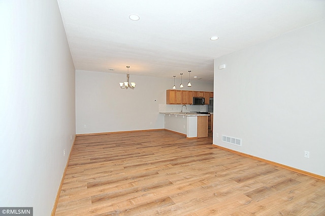 unfurnished living room featuring sink, light hardwood / wood-style flooring, and a chandelier