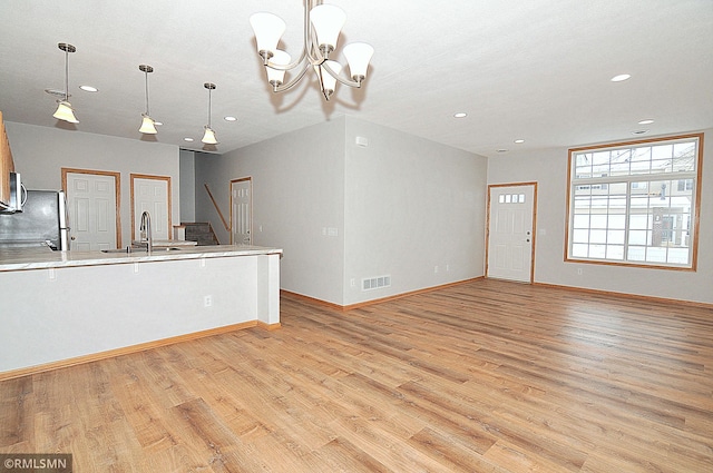 kitchen with hanging light fixtures, sink, stainless steel refrigerator, and light wood-type flooring