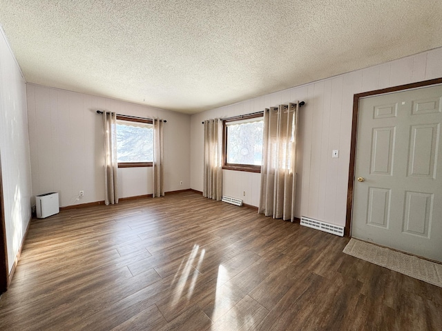 empty room with a wealth of natural light, a textured ceiling, and dark wood-style floors