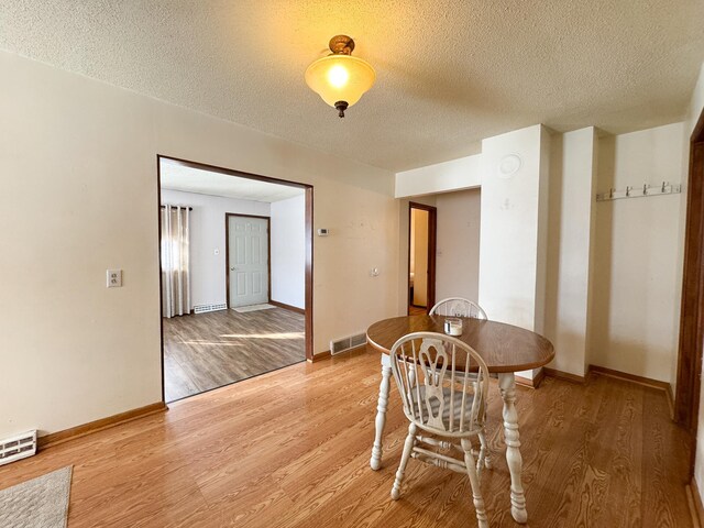 dining area with a textured ceiling, baseboards, visible vents, and light wood-type flooring