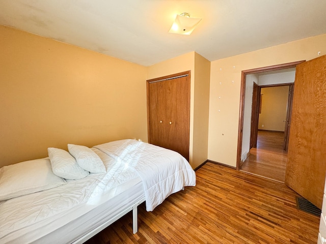 bedroom with a closet, visible vents, baseboards, and wood finished floors