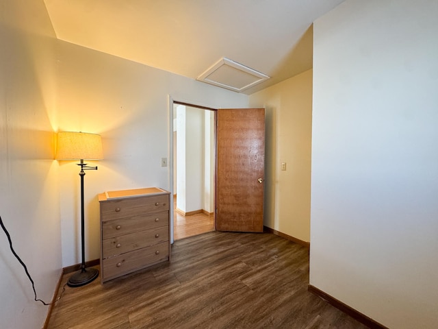 unfurnished bedroom featuring attic access, dark wood-type flooring, and baseboards