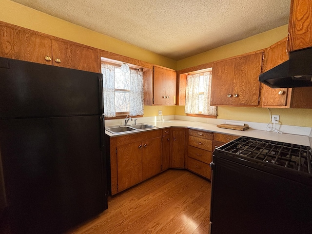 kitchen with light wood-style flooring, a sink, a textured ceiling, brown cabinetry, and black appliances