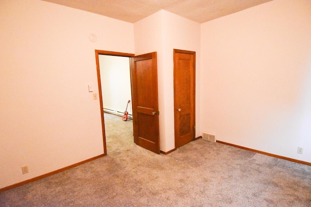 empty room featuring a baseboard heating unit and light colored carpet