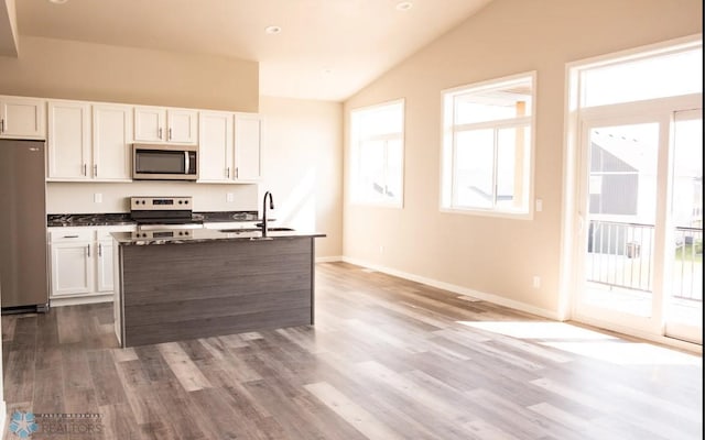 kitchen with lofted ceiling, plenty of natural light, white cabinets, and appliances with stainless steel finishes