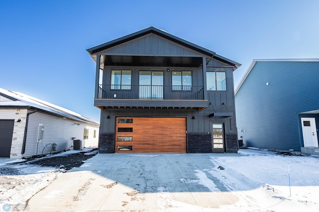 view of front of property featuring a balcony, stone siding, an attached garage, central AC, and board and batten siding