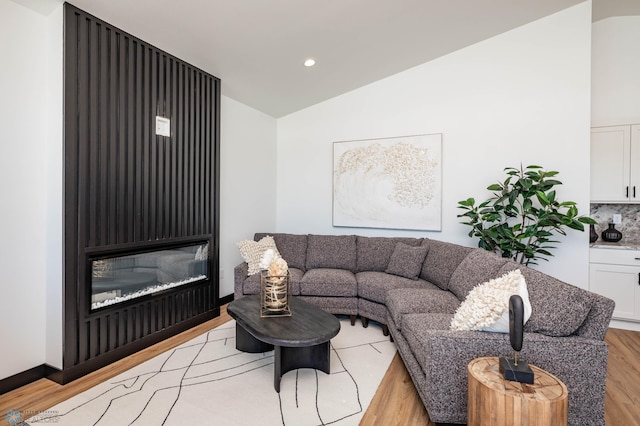 living area featuring light wood finished floors, recessed lighting, vaulted ceiling, and a glass covered fireplace