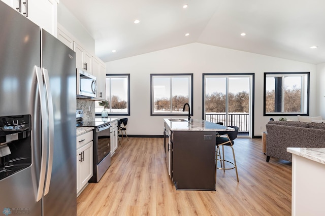 kitchen featuring stainless steel appliances, light stone countertops, a center island with sink, and white cabinetry