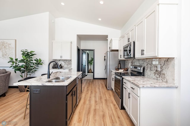 kitchen with lofted ceiling, a breakfast bar area, stainless steel appliances, a sink, and white cabinets