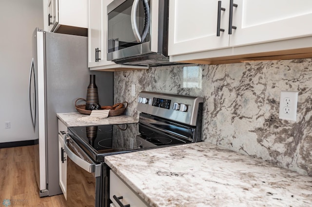 kitchen with light wood finished floors, tasteful backsplash, appliances with stainless steel finishes, white cabinets, and light stone countertops