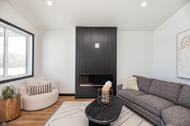 living room featuring a large fireplace, baseboards, light wood-style flooring, and recessed lighting