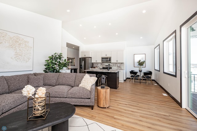 living room with high vaulted ceiling, recessed lighting, baseboards, and light wood finished floors