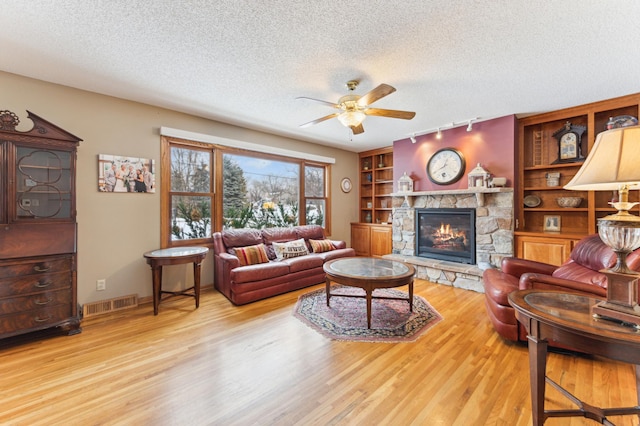 living room featuring light wood-type flooring, a fireplace, ceiling fan, a textured ceiling, and rail lighting