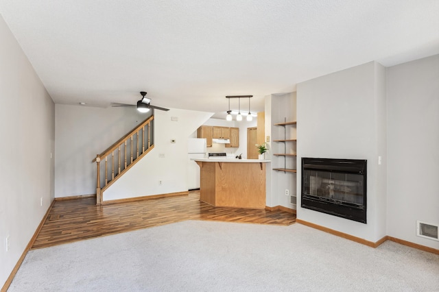 unfurnished living room with visible vents, baseboards, a glass covered fireplace, ceiling fan, and stairs