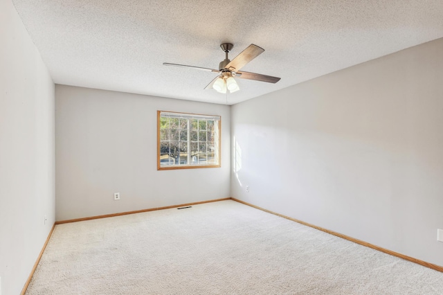 empty room with light colored carpet, ceiling fan, a textured ceiling, and baseboards