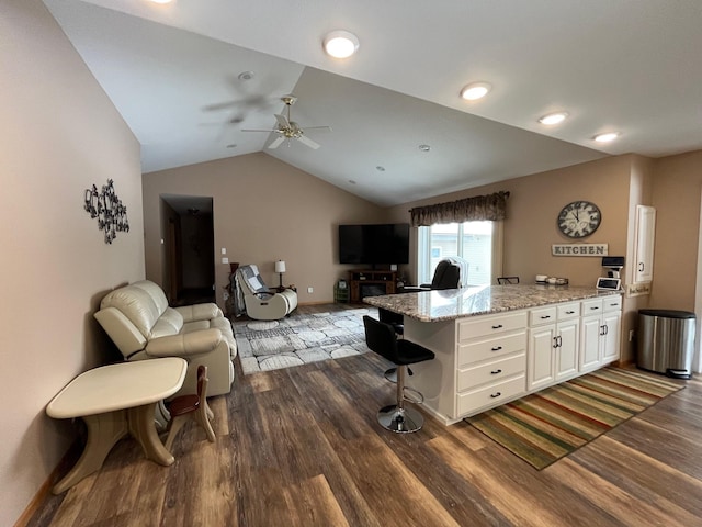 kitchen with lofted ceiling, a breakfast bar area, dark hardwood / wood-style floors, light stone countertops, and white cabinets